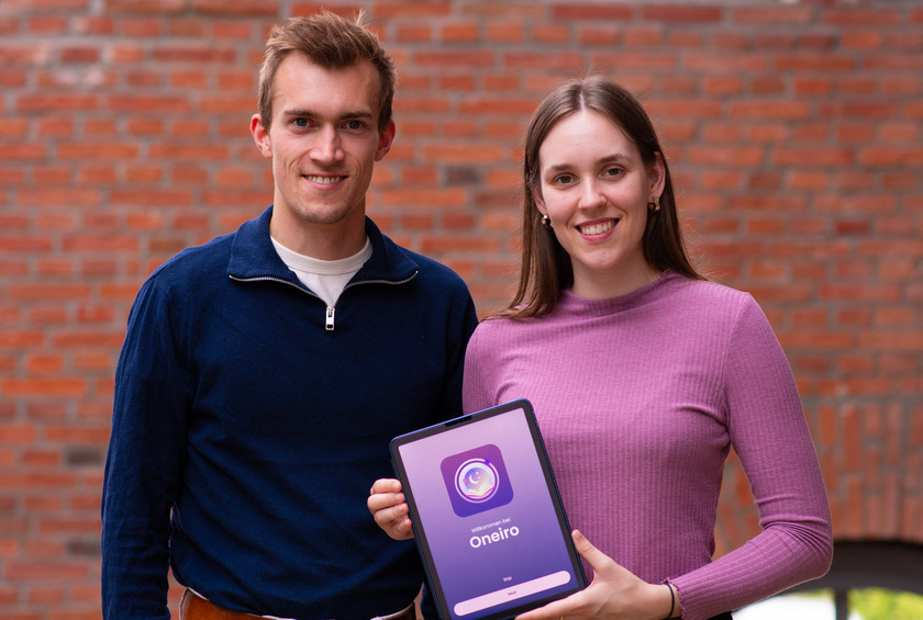 Auf dem Foto sind ein junger Mann (links) und eine junge Frau (rechts) zu sehen. Die Frau hält ein Tablet in der Hand, auf der eine App geöffnet ist. Es steht groß Oneiro auf dem Tablet.