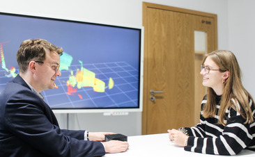 Zwei Menschen unterhalten sich vor einem Schaubild. 