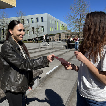 Interviewsituation mit zwei Studierenden, es wird ein Zettel gezogen mit einer Frage, die daraufhin eingeschätzt werden soll