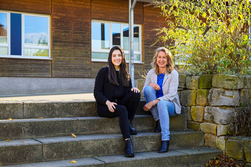 Josefa Davalos und Pia Röhner sitzen nebeneinander auf einer Treppe auf dem Außengelände der HHO.