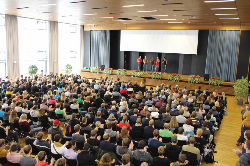 Das Bild zeigt einen großen Raum, in dem viele besetzte Stuhlreihen zu sehen sind.