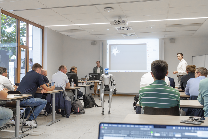 Ein humanoider Roboter läuft durch einen Mittelgang in einem Vorlesungsraum, der mit Menschen gefüllt ist. 