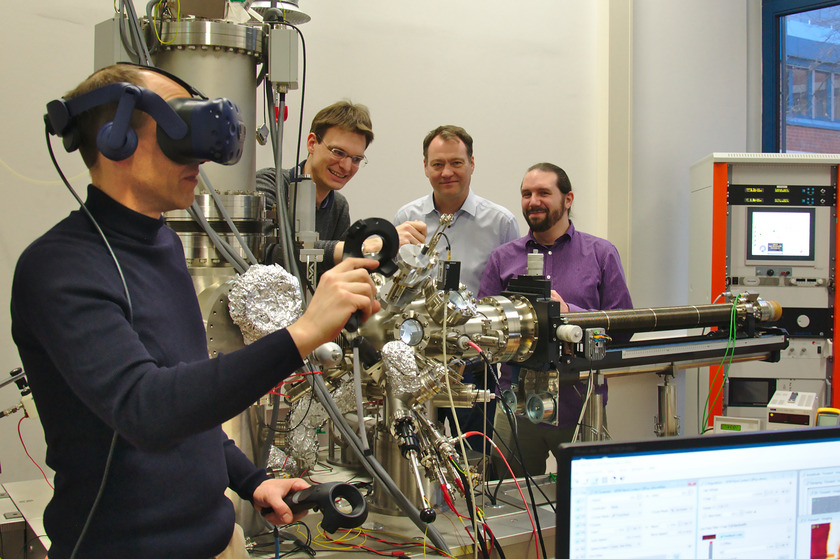 Im Fokus steht ein Mann mit VR-Brille im Labor, drei weitere Männer tüfteln im Hintergrund