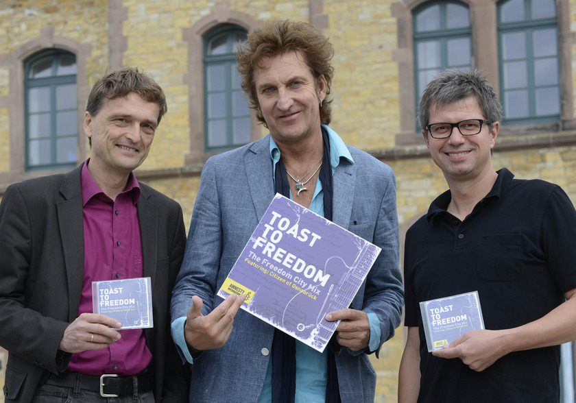 Auf dem Bild sieht man drei Männer, die ein überdimensionales CD-Cover in den Händen halten.