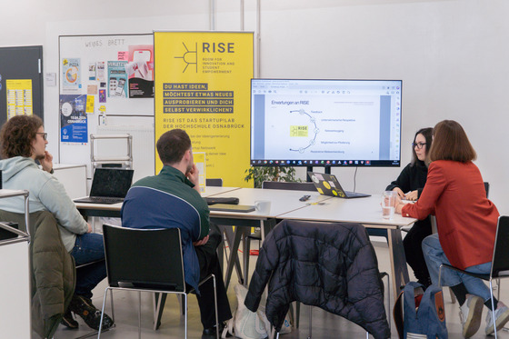 Teilnehmende sitzen in einem Workshopraum und verfolgen eine Präsentation an einem Bildschirm.
