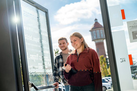 Zwei Studierende betreten ein Gebäude am Campus Lingen. Im Hintergrund ist der Wasserturm am Bahnhof Lingen zu sehen.Campus Lingen
