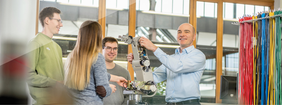 Professor erklärt Studierenden in einem Labor einen Roboterarm.