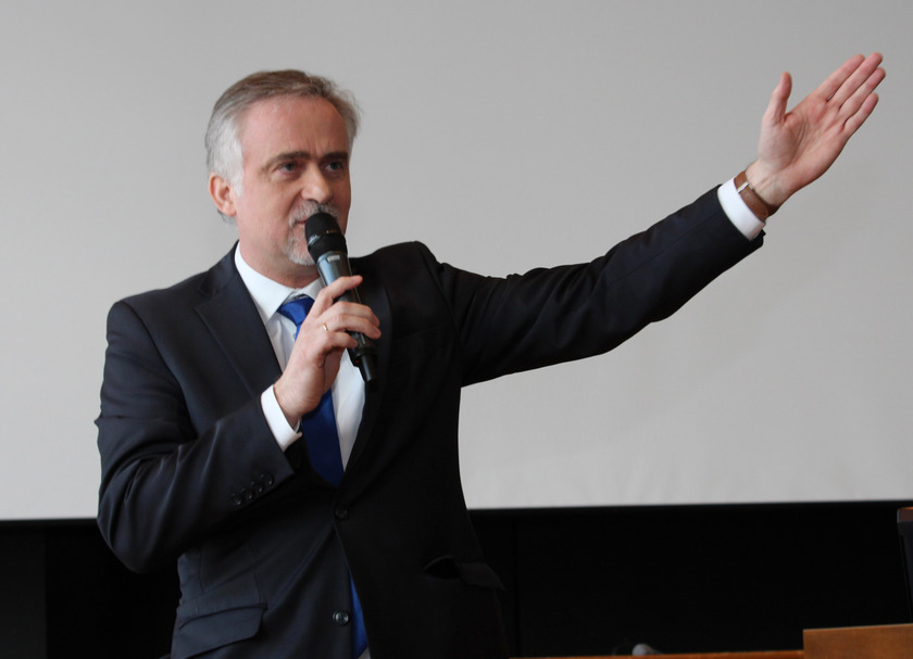 Ein Mann im Anzig spricht in ein Mikrophon und streckt den linken Arm in die Höhe.