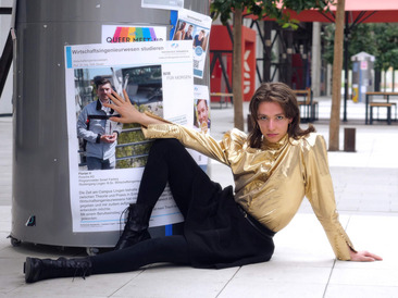 Nila sitzt auf dem Boden vor einer Litfaßsäule