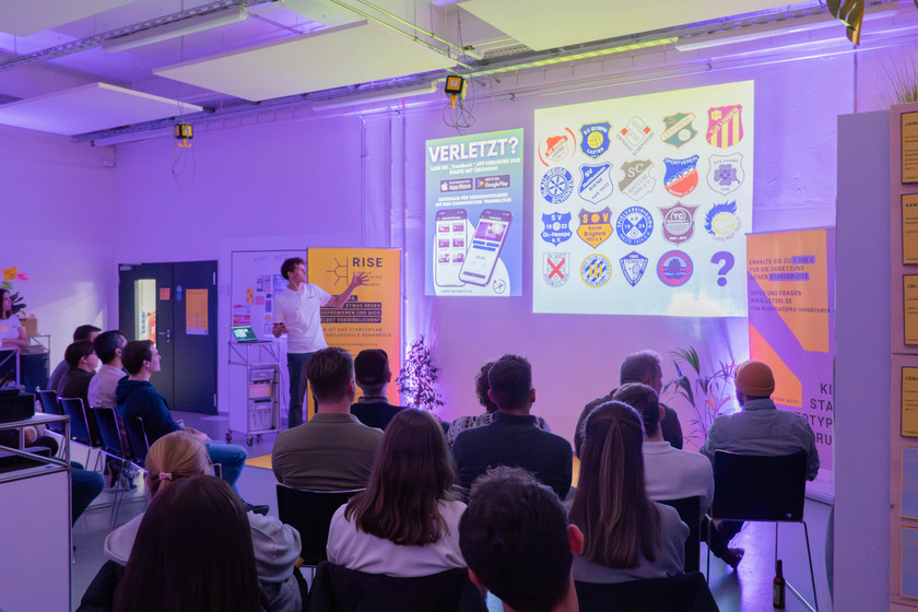 Das Bild zeigt den Gründer Henry Sievers wie er anhand einer Präsentation einer Gruppe von sitzenden Personen seine Startup-Idee vorstellt.