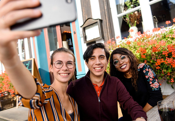 Auch in der Freizeit bietet Lingen jede Menge Cafés und Treffpunkte für Studierende. Drei Studierende sitzen auf der Bank und machen ein Selfie.